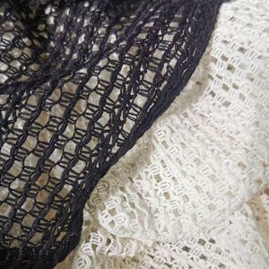 Pode incluir: Close-up de tecido de trama aberta preto e branco. O tecido preto está à esquerda, com uma borda definida. O tecido branco está à direita, com um padrão de trama aberta semelhante. As texturas criam um contraste.