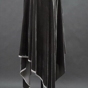 May include: A draped, dark gray velvet fabric with a subtle sheen. The fabric is hanging, with a contrasting white trim outlining the edges. The overall effect is elegant and flowing, suggesting a garment or decorative textile.
