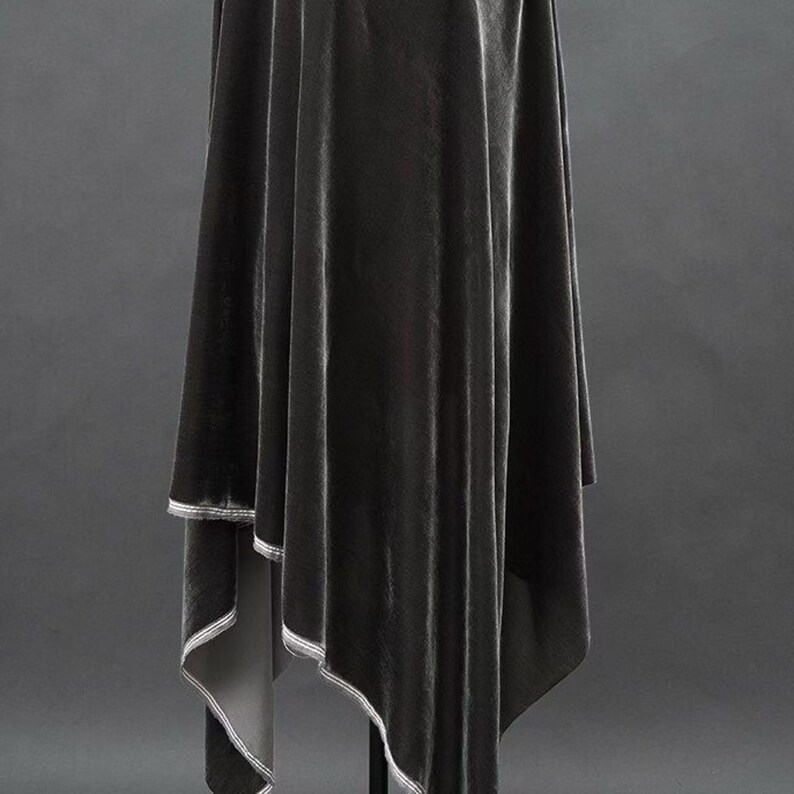 May include: A draped, dark gray velvet fabric with a subtle sheen. The fabric is hanging, with a contrasting white trim outlining the edges. The overall effect is elegant and flowing, suggesting a garment or decorative textile.