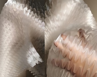 Puede incluir: Obra de arte abstracta que presenta un material blanco translúcido con un patrón en zigzag. El material está doblado y en capas, creando un efecto tridimensional texturizado. La iluminación resalta los intrincados pliegues y sombras, dando profundidad a la pieza.