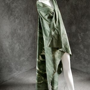 Puede incluir: Prenda de tela verde oliva drapeada sobre un maniqu&iacute; blanco. La tela tiene un aspecto jaspeado, te&ntilde;ido anudado, con zonas verdes m&aacute;s oscuras. La prenda est&aacute; drapeada sobre el hombro y el brazo del maniqu&iacute;.