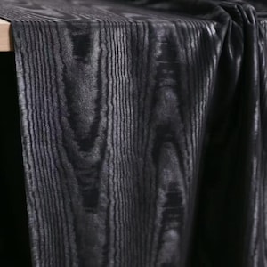 Puede incluir: Una pieza de tela con un patr&oacute;n de veta de madera en negro oscuro y gris carb&oacute;n. El material muestra una orientaci&oacute;n vertical de la veta, con l&iacute;neas negras profundas que se alternan con tonos grises para imitar la apariencia de la madera.