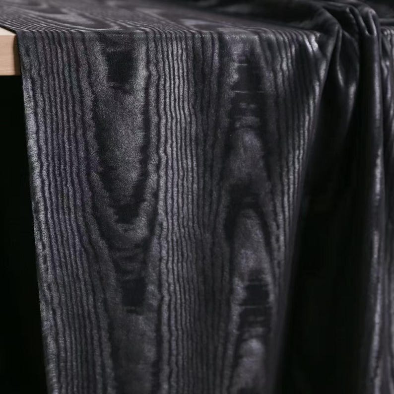 Puede incluir: Una pieza de tela con un patr&oacute;n de veta de madera en negro oscuro y gris carb&oacute;n. El material muestra una orientaci&oacute;n vertical de la veta, con l&iacute;neas negras profundas que se alternan con tonos grises para imitar la apariencia de la madera.