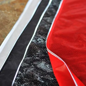 May include: An abstract image showcasing various textures and colors. A section of red, glossy material is visible, alongside black, white, and brown sections. The black section has a snakeskin pattern. Each section is separated by a thin, silver trim.