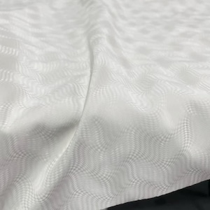 Könnte beinhalten: Nahaufnahme eines weißen Stoffes mit einem strukturierten, wellenartigen Muster. Der Stoff scheint gefaltet zu sein, wodurch Schatten entstehen und das komplizierte Design hervorgehoben wird. Das Material hat einen subtilen Glanz, der auf ein hochwertiges Textil hindeutet.