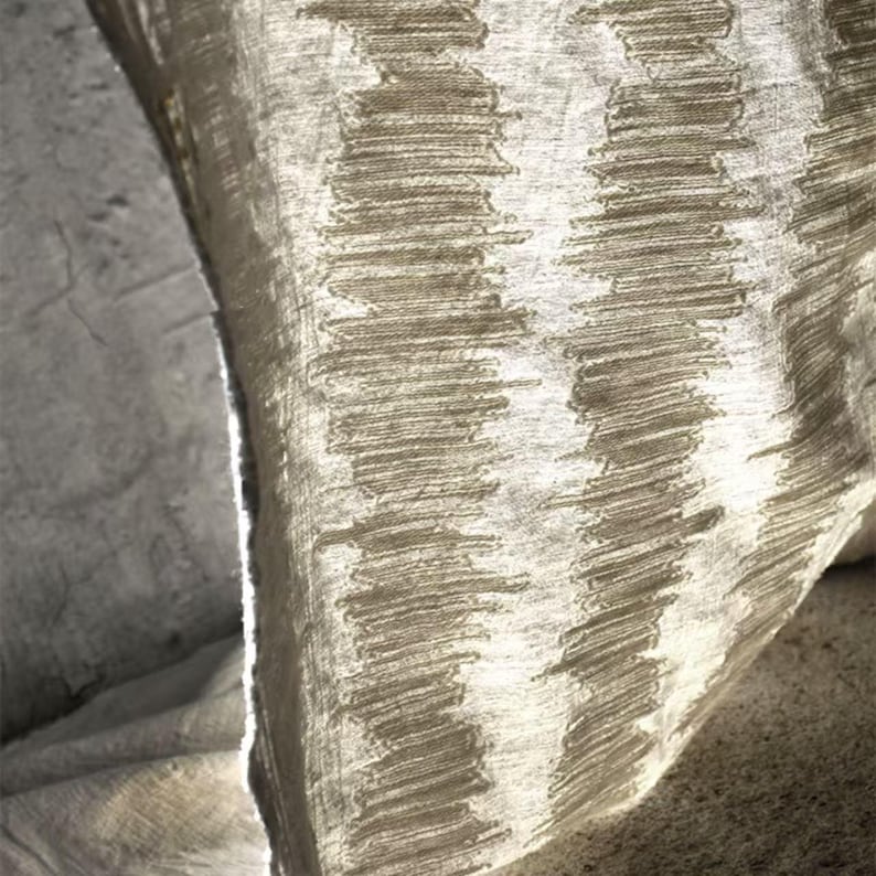 May include: Close-up of a textured fabric with a repeating pattern of vertical, stitched lines. The fabric has a neutral color palette, with shades of beige and off-white. The texture appears soft and slightly wrinkled, suggesting a linen or similar material.