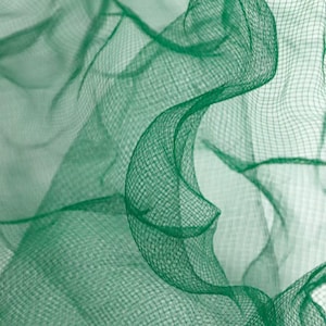 May include: Close-up of a flowing, emerald green netting fabric. The fabric is semi-transparent with a fine, grid-like weave. The image highlights the texture and the way the fabric drapes and curves, creating a sense of movement and depth.