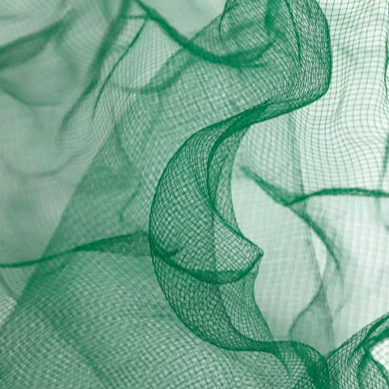 May include: Close-up of a flowing, emerald green netting fabric. The fabric is semi-transparent with a fine, grid-like weave. The image highlights the texture and the way the fabric drapes and curves, creating a sense of movement and depth.