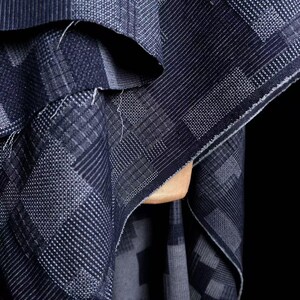 May include: A dark blue fabric featuring a geometric pattern of squares and rectangles with varying textures. The design consists of alternating blocks of fine horizontal lines, vertical stripes, and dotted grids, creating a complex, layered visual effect.