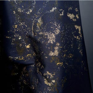 May include: Close-up of a navy blue fabric with a textured surface. The fabric is adorned with irregular gold leaf-like patterns, creating a luxurious and artistic appearance. The folds in the fabric add depth and dimension.