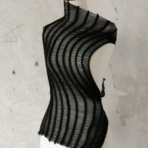 May include: Black, sleeveless top with a high neckline and a unique, wavy design. The fabric appears to be a sheer, woven material, creating a textured effect. The top is displayed on a mannequin against a neutral background.