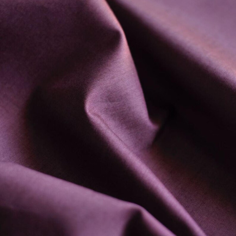 May include: Close-up of a deep purple fabric with soft folds and subtle texture. The fabric appears to be smooth and drapes naturally, creating shadows and highlights. The color is rich and saturated.