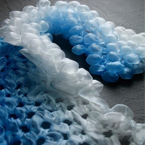 Könnte beinhalten: Ein dekoratives, abstraktes Kunstwerk in Blau- und Weißtönen. Das Stück scheint aus einem weichen, stoffartigen Material mit einer gerüschten, wolkenartigen Textur zu bestehen. Die Farbe wechselt von einem tiefen Blau zu einem sanften Weiß.
