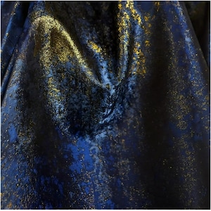 Pode incluir: Close-up de um tecido texturizado com uma base azul escuro e flocos dourados. O tecido tem uma aparência brilhante e metálica, com áreas de sombra profunda e destaques. O efeito geral é luxuoso e elegante.