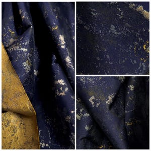 May include: Close-up of a textured fabric with a dark navy blue base and gold and silver metallic accents. The fabric is folded, revealing the texture and sheen of the material. The overall effect is a luxurious, abstract design.
