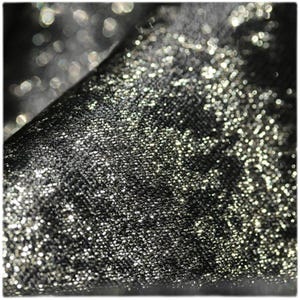 Puede incluir: Primer plano de una tela negra con una textura brillante y con purpurina. La tela est&aacute; doblada, revelando un juego de luces y sombras. La superficie est&aacute; cubierta de diminutas part&iacute;culas reflectantes.