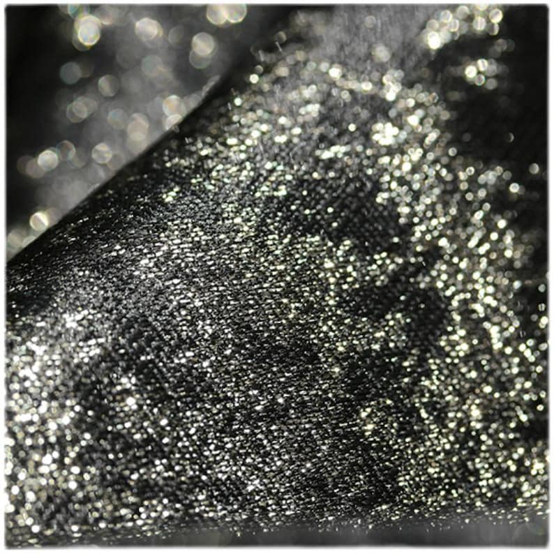 Puede incluir: Primer plano de una tela negra con una textura brillante y con purpurina. La tela est&aacute; doblada, revelando un juego de luces y sombras. La superficie est&aacute; cubierta de diminutas part&iacute;culas reflectantes.