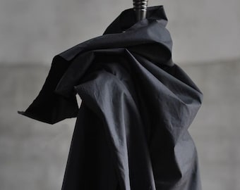 May include: A dark navy blue fabric draped over a wooden stand. The fabric is bunched and folded, creating shadows and texture. The stand has a dark, decorative top. The background is a neutral gray.