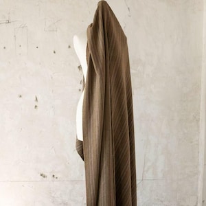 May include: Brown fabric with vertical stripes draped over a white mannequin. The fabric has a textured appearance and a warm, earthy color palette. The stripes vary in width and shade, creating visual interest.