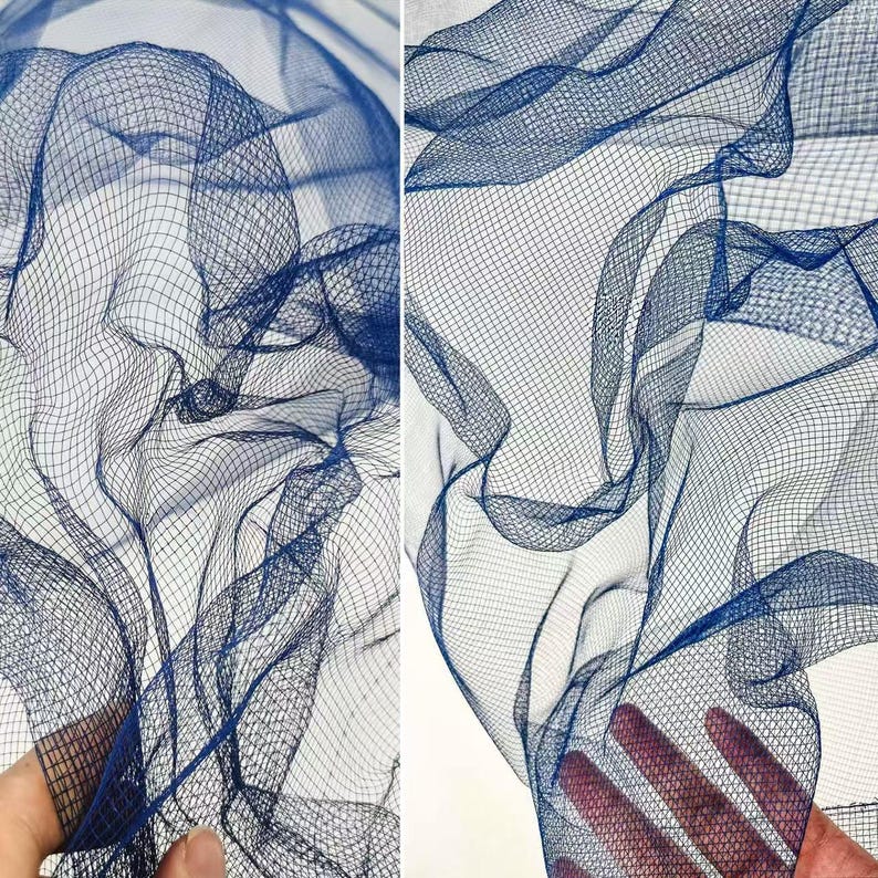 May include: Close-up of a navy blue mesh fabric with a fine grid pattern. The fabric is gathered and draped, creating soft folds and shadows. The texture is visible, and the color is consistent throughout the image.