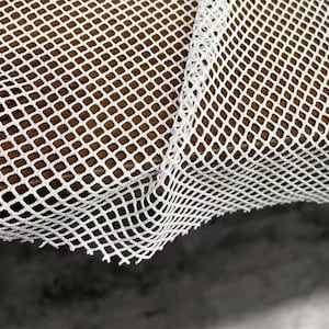 Può includere: Primo piano di tessuto a rete bianco a trama aperta. La rete ha un motivo a rombi ed è drappeggiata su una superficie di legno. La trama del tessuto e le venature della superficie in legno sono visibili.