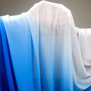 May include: A sheer fabric with a gradient of colors, transitioning from deep blue to light blue and finally to white. The fabric is draped, creating soft folds and a flowing appearance. The material appears lightweight and translucent.