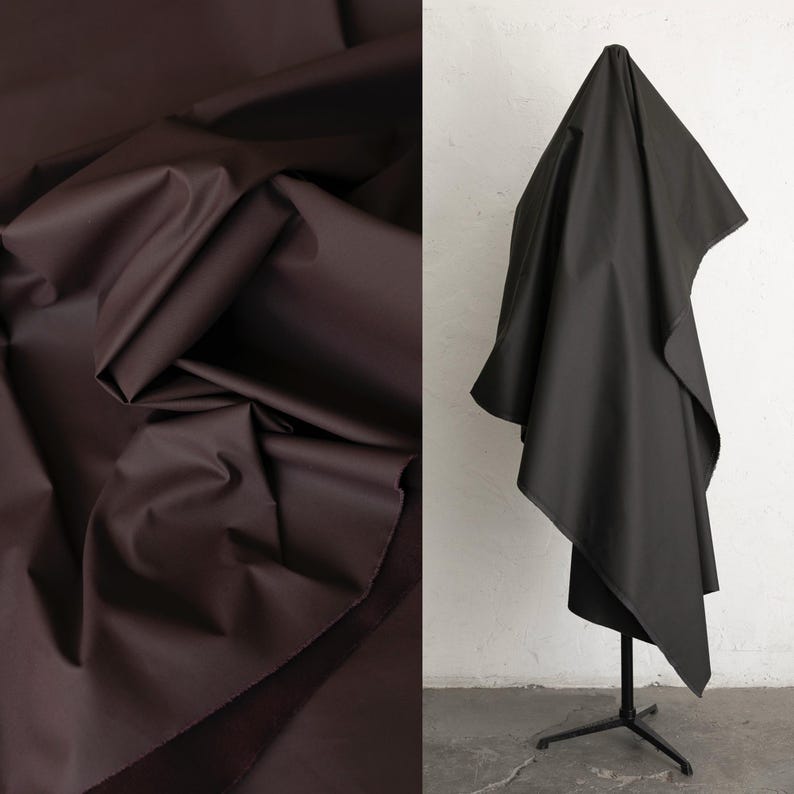 May include: Two fabric samples. One is a dark brown, folded and draped. The other is a black fabric draped over a black metal stand. The fabrics appear to be smooth and possibly a medium weight.