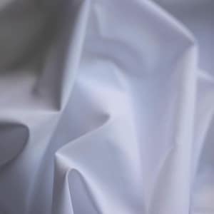 May include: Close-up of white fabric with soft folds and shadows. The fabric appears smooth and possibly silky, with a subtle gradient of light and shadow creating depth. The overall effect is clean and minimalist.