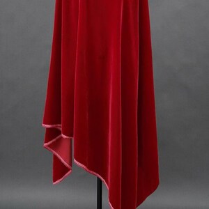May include: A flowing, deep red velvet fabric with a subtle sheen. The edges are finished with a delicate white trim. The fabric drapes elegantly, suggesting a garment or decorative textile.