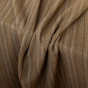 May include: Close-up of a textured fabric with a brown and tan striped pattern. The fabric is draped, showing folds and variations in the weave. The material has a subtle sheen, suggesting a blend of fibers.