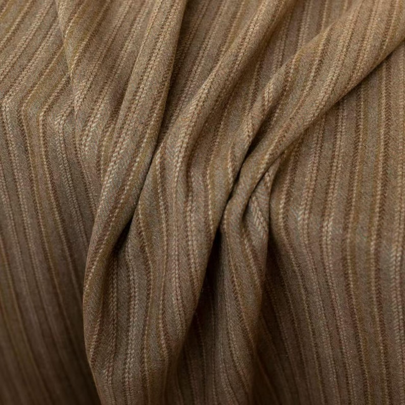 May include: Close-up of a textured fabric with a brown and tan striped pattern. The fabric is draped, showing folds and variations in the weave. The material has a subtle sheen, suggesting a blend of fibers.