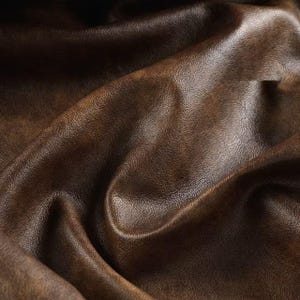 May include: Close-up of a textured, brown leather material with a distressed appearance. The leather has a rich, warm color with variations in tone, and visible grain and folds.