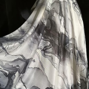 Puede incluir: Tela fluida con un diseño estilo acuarela en tonos grises y blancos. El patrón se asemeja a un paisaje con árboles abstractos y líneas fluidas, creando una estética suave y artística.