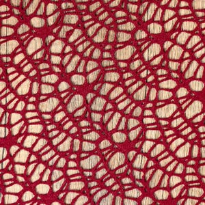 May include: Close-up of a red, open-weave fabric with a pattern of interconnected, irregular shapes. The fabric is set against a light-colored, wood-grain background, creating a contrast in textures and colors. The design resembles a network or web.