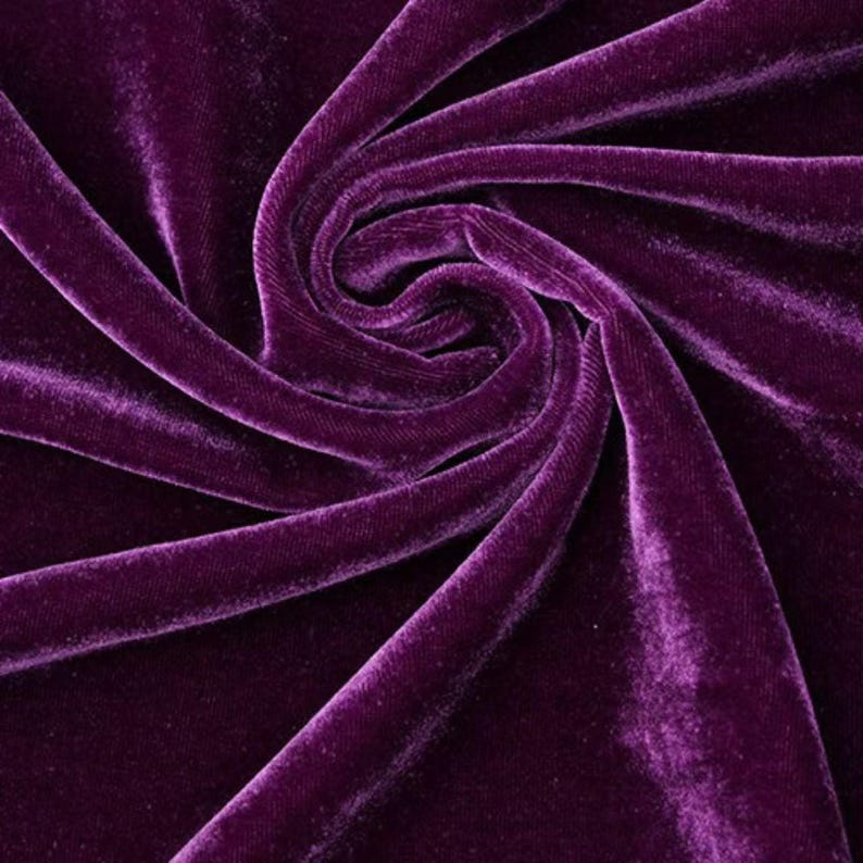 May include: Close-up of a swirl of deep purple velvet fabric. The fabric has a soft, plush texture with visible folds and shadows, creating a rich, luxurious appearance. The colour is a vibrant, saturated shade of purple.