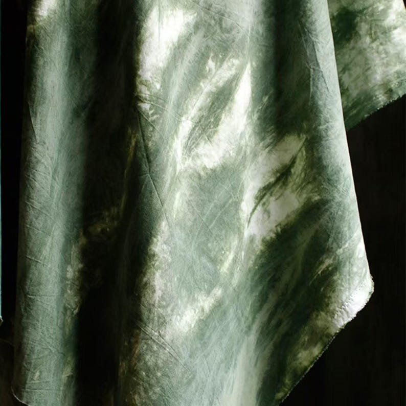 Puede incluir: Primer plano de una tela te&ntilde;ida con tinte verde y blanco. La tela tiene un aspecto fluido y texturizado con una mezcla de tonos verdes claros y oscuros. El dise&ntilde;o crea un efecto veteado, con vetas blancas.