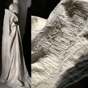 May include: A draped, off-white fabric with a textured surface is displayed on a mannequin. The fabric has a woven appearance with visible threads and raised, patterned details. The overall aesthetic is soft and natural, suggesting a focus on texture and organic materials.