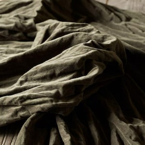 Könnte beinhalten: Nahaufnahme eines olivgrünen Stoffes mit weichen Falten und strukturiertem Aussehen. Der Stoff scheint Leinen oder ein ähnliches Material zu sein, mit einer leicht zerknitterten Textur. Die Beleuchtung erzeugt Schatten und Glanzlichter, die die Textur des Stoffes hervorheben.