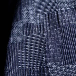 May include: A dark blue fabric featuring a geometric patchwork pattern composed of alternating squares. The design includes sections with vertical stripes, horizontal lines, and fine grid textures, all rendered in varying shades of navy blue.