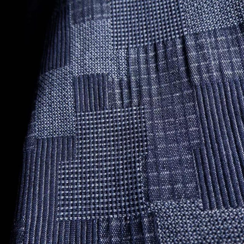 May include: A dark blue fabric featuring a geometric patchwork pattern composed of alternating squares. The design includes sections with vertical stripes, horizontal lines, and fine grid textures, all rendered in varying shades of navy blue.