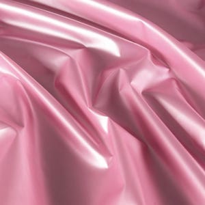 Peut inclure: Gros plan sur un tissu rose brillant avec des plis et des reflets doux. Le matériau a une surface lisse et réfléchissante, créant une sensation de profondeur et de texture. L'effet général est élégant et luxueux.