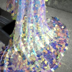 May include: Iridescent fabric with large, round sequins in shades of purple, blue, yellow, and green. The sequins are attached to a sheer, white fabric, creating a shimmering effect. The fabric appears to be draped or flowing.