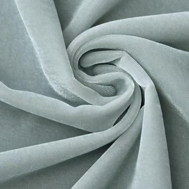 May include: Close-up of a soft, flowing fabric in a muted teal color. The material is draped and swirled, creating a sense of movement and texture. The fabric appears to be velvet or a similar plush material, ideal for apparel or home decor.