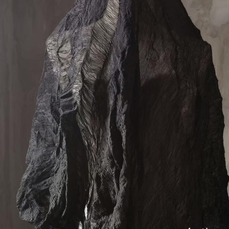 May include: A draped, textured fabric in shades of black and gray. The material appears to have a layered, rippled design, creating a sense of depth and movement. The fabric is likely used for clothing or decorative purposes.