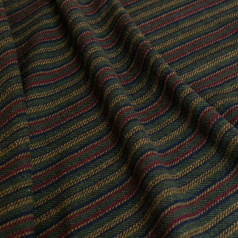 May include: Close-up of a textured fabric with diagonal stripes. The fabric features a pattern of alternating stripes in dark green, navy blue, red, and gold. The fabric is draped, showing the texture and folds of the material.