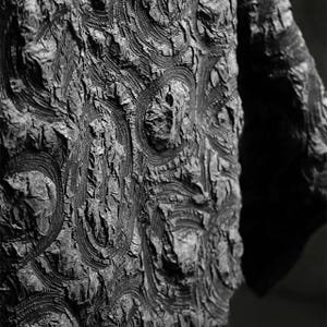 May include: Detailed shot of a dark grey fabric with a textured surface. The fabric features a repeating pattern of raised, circular motifs, creating a tactile and visually interesting design.