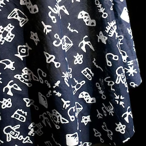 May include: Dark navy fabric with a repeating white pattern of abstract shapes and symbols. The fabric is draped, showing folds and texture. The design is reminiscent of ancient writing or hieroglyphs.