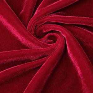 May include: Close-up of a deep red velvet fabric with a soft, lustrous texture. The fabric is arranged in swirling folds, creating a dynamic pattern of light and shadow. The rich colour and tactile quality suggest luxury and elegance.