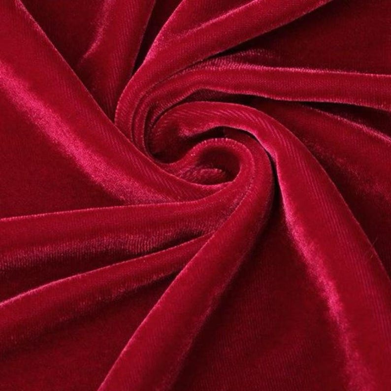 May include: Close-up of a deep red velvet fabric with a soft, lustrous texture. The fabric is arranged in swirling folds, creating a dynamic pattern of light and shadow. The rich colour and tactile quality suggest luxury and elegance.