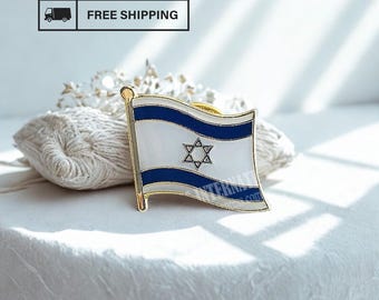 May include: A gold-toned pin featuring the flag of Israel. The flag design includes a white background, two horizontal blue stripes, and a blue Star of David in the center. The pin is set against a soft, textured background.